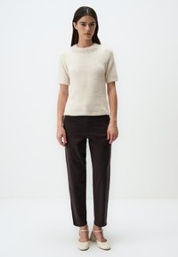 Pull en tricot ivoire à manches courtes avec une texture douce, associé à un pantalon sombre et des chaussures de couleur claire avec des brides à la cheville.