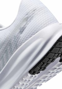 Gros plan de la basket blanche montrant une tige en tissu texturé, une semelle intermédiaire rembourrée et un motif de bande de roulement noir sur la semelle extérieure.