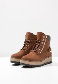 Brązowe zamszowe botki za kostkę o teksturowanym wykończeniu, z wiązaniem z przodu, bocznymi zamkami błyskawicznymi i gumowymi podeszwami z lekkim klinem.