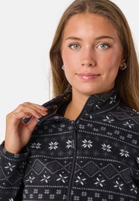 Polarowy dres w czarnym kolorze z białymi wzorami w śnieżynki i geometrę, z pełnym zamkiem z przodu, wysokim kołnierzem i miękką teksturą.