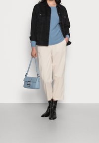 Kobieta w czarnej dżinsowej kurtce, niebieskim swetrze, kremowych szerokich spodniach, czarnych botkach za kostkę, trzymająca jasnoniebieską torebkę przy boku.