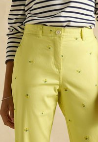 Kollane puuvillane püksid, millel on tikitud sidruni motiivid ja nööpkinni, koos tumesinise ja valge triibulise pikakätise särgiga.