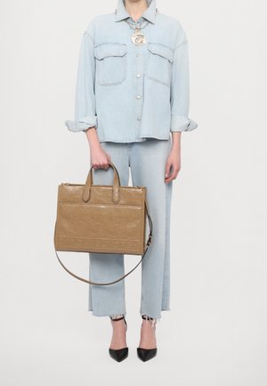 Chemise en denim bleu clair à boutons, jeans évasés assortis, et un sac à main texturé beige avec des poignées supérieures et une bandoulière amovible. Escarpins noirs pointus.