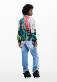 Suéter colorido y extragrande con patrones abstractos, combinado con jeans holgados azul claro y botines negros de tacón. Tejido texturizado.