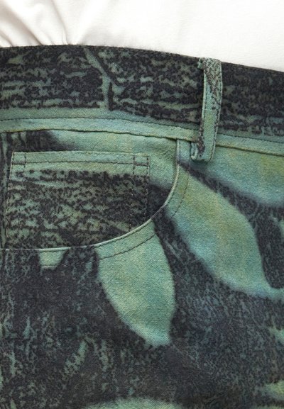 Κοντινό πλάνο σε ύφασμα με καμουφλάζ πράσινου και μαύρου χρώματος που δείχνει τσέπη, θηλιά για ζώνη και ραφές.