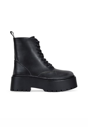 Botas de tobillo de cuero negro con puntera redondeada, cierre de cordones en la parte delantera y suela de plataforma gruesa. Cuenta con un tirador y acentos de costura texturizada.