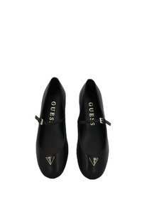 Scarpe Mary Jane nere con piccolo logo triangolare Guess sulla punta e cinturini laterali regolabili, mostrate dall'alto su sfondo bianco.