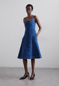 Denim jurk met een aansluitend lijfje en een uitlopende rok, voorzien van verstelbare bandjes, zijzakken en contrasterende stiksels. Donkerblauwe kleur.