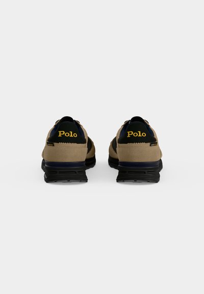 Ζευγάρι μπεζ και μαύρα sneakers Polo με μαύρες σόλες, βλεπόμενα από πίσω, που δείχνουν το κίτρινο λογότυπο Polo στην περιοχή της φτέρνας.