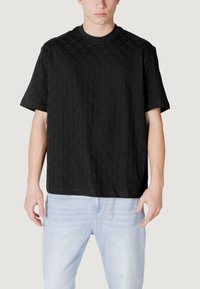 T-shirt nera a maniche corte con un motivo a diamante strutturato, scollo rotondo e vestibilità comoda, abbinata a jeans in denim azzurro chiaro.