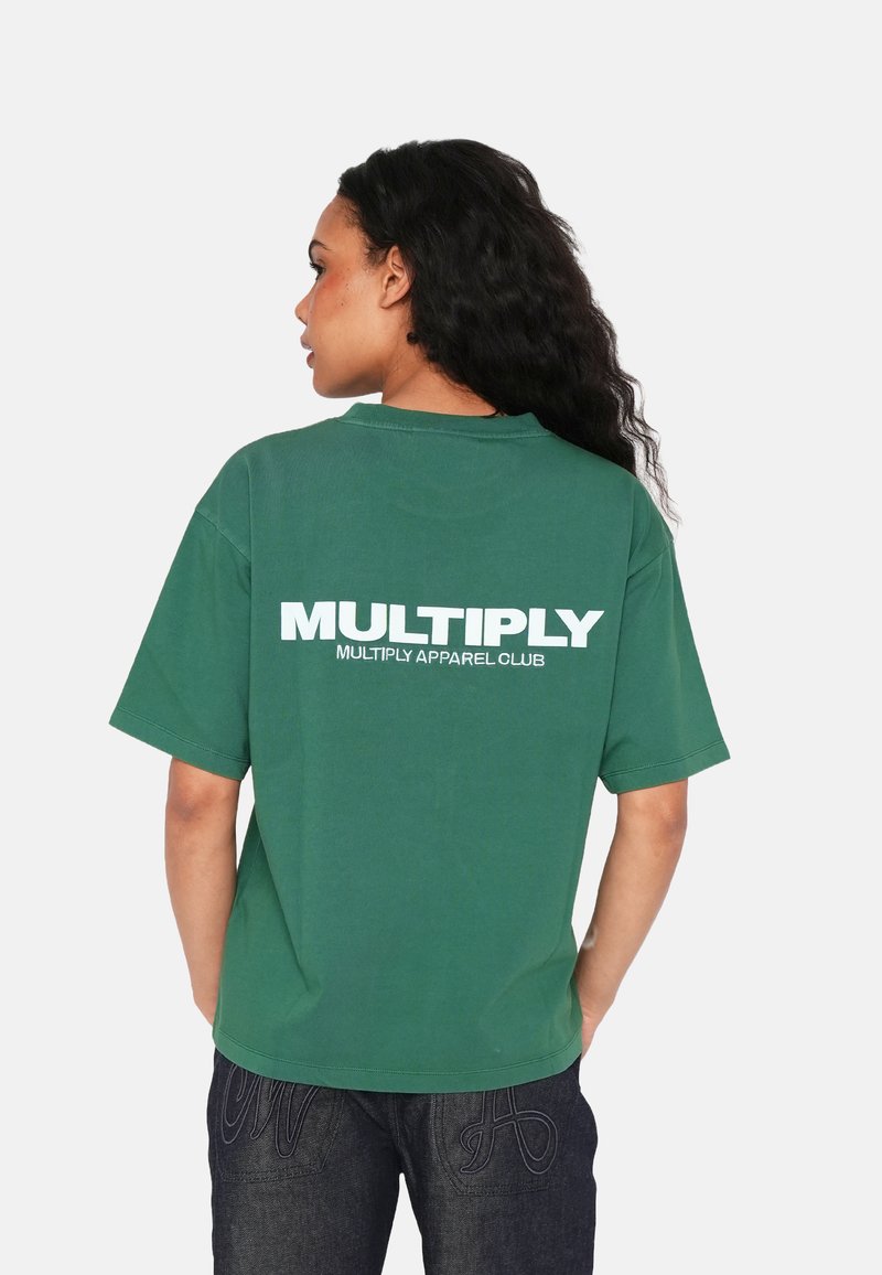 Camiseta verde de gran tamaño hecha de algodón, con cuello redondo y mangas cortas. Texto en la parte posterior: "MULTIPLY APPAREL CLUB" en letras blancas en negrita.