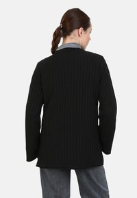 Schwarzer gestreifter langer Mantel mit strukturiertem Design und texturiertem Stoff. Verfügt über lange Ärmel und eine taillierte Silhouette.