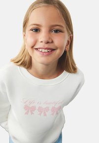 Witte sweatshirt met de tekst "Het leven is mooi" in het roze, versierd met drie roze strikillustraties. Zachte stof, ronde halslijn.
