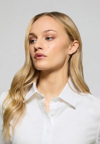 Vitt skjort med klassisk krage, som har en liten logotyp på bröstet. Slät bomullstyg, figursydd design och långa ärmar.