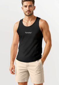 Schwarzes ärmelloses Tanktop mit dem weißen "Neverless"-Logo, kombiniert mit hellbeigen Shorts. Glatter Stoff, runder Ausschnitt, taillierte Passform.
