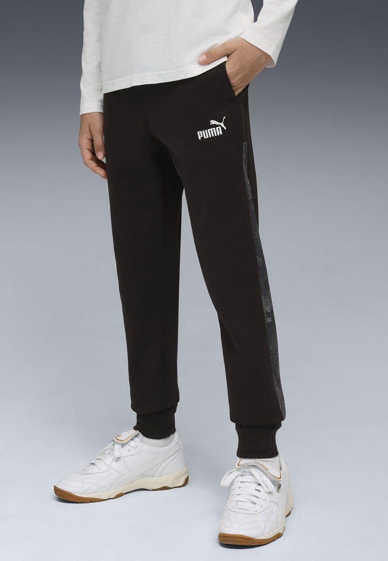 Zwarte sportbroek met elastische boorden, uitgerust met een wit Puma-logo en een grijze zijstreep. De stof lijkt zacht en comfortabel.