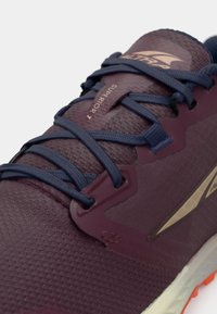Ciemnofioletowe buty do biegania z teksturowaną cholewką, granatowymi sznurowadłami i jasnoszarym bieżnikiem. Posiadają wzmocniony czubek oraz logo na boku.
