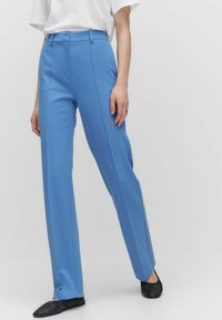 Blå skräddarsydda byxor i ett lätt tyg. Har hög midja, raka ben och subtila framfickor. Matchas med svarta platta skor.