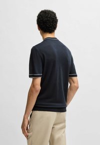 Navy short-sleeve sweater made of soft fabric with white-accented cuffs and collar, featuring a relaxed fit and classic design.