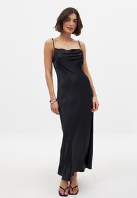 Black satin dress with a cowl neckline, slim straps, and a floor-length silhouette. Smooth texture creates a sleek, elegant look.