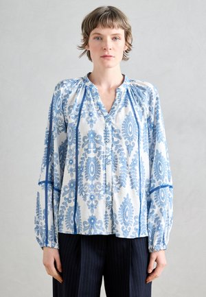 Kerge, nööpidega pluus siniste lillemustritega valgel taustal. Pikkade varrukatega, millel on elastsed mansetid, ja v-kaelusega.