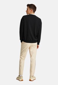 Schwarzer Sweatshirt mit rundem Hals, eng anliegenden Bündchen, getragen mit cremefarbenen Chinos und beigen Sneakers. Glatte Textur und schlichtes Design.