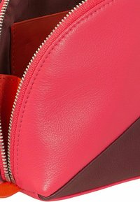 Bolso de cuero rosa con un acento triangular en marrón oscuro en contraste, que presenta una cremallera de metal y una textura suave. En el interior muestra un forro naranja.