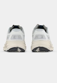 Hvite og grå atletiske sko med en klumpete silhuett, mesh-overdeler og teksturerte gummisåler. Har logo-accenter på baksiden.