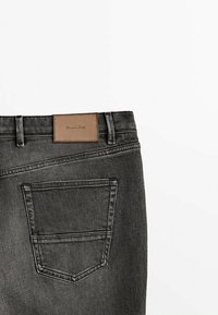 Grå denimjeans med en rektangulär läderlapp på midjan med präglat varumärkesnamn och en enda bakficka med sömnad.