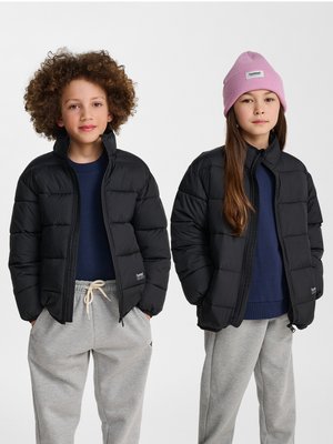 Zwei Kinder tragen schwarze Daunenjacken, marineblaue Oberteile und graue Jogginghosen; eines der Kinder hat lockiges Haar, das andere trägt eine rosa Mütze.