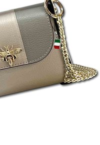 Beige en grijze nep leren crossbody tas met een gouden bijembleem, kettinghengsel en charm van de Italiaanse vlag. Heeft een klep sluiting en een getextureerd oppervlak.