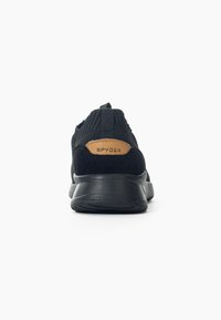 Scarpa sportiva nera con tomaia in maglia testurizzata, un accento in pelle beige sul tallone e una spessa suola in gomma nera.
