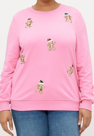 Roze sweatshirt met lange mouwen met met pailletten versierde peperkoekmannetjes die rode en groene kerstmanmutsen dragen, gedragen met blauwe jeans, getoond van nek tot heupen.