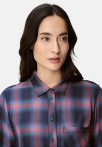 Blue and red plaid shirt with a button-down collar, front pocket, and textured fabric. Features rounded hem and subtle print details.