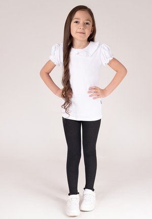 Biała bluzka z krótkim rękawem i falbanianym kołnierzem, zestawiona z czarnymi prążkowanymi legginsami. Stylizację uzupełniają białe trampki.