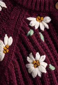 Strickpullover in Maroon mit weißen und gelben gestickten Blumen sowie grünen Blättern; mit einem strukturierten Rippenmuster und hohem Kragen.