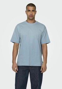 Helles blaues Baumwoll-T-Shirt mit Rundhalsausschnitt, kurzen Ärmeln und lockerer Passform. Kombiniert mit dunkelblauen Jeans.