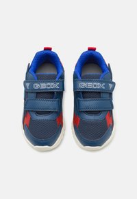 Sneakers albastre și roșii dintr-un amestec de plasă și piele, cu curele Velcro, tălpi albe și un model texturat. Logo-ul brandului pe curele.