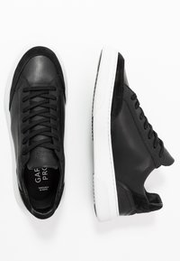 Svarta sneakers med släta läder- och mockadetaljer, rund tå, snörningsdesign och vit gummisula med texturerade detaljer.