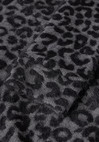 Grått stickat tyg med ett svart leopardmönster. Mjuk textur med något upphöjda fibrer. Geometriska former genom hela designen.