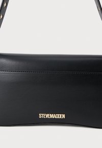 Geantă din piele artificială neagră, cu o textură netedă, având un logo auriu "STEVE MADDEN" și un mâner subțire, reglabil.