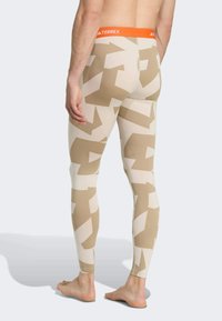 Beige leggings with abstract tan patterns, featuring an orange waistband with "TERREX" branding. Made from stretchy, lightweight fabric.