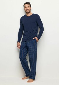 Marineblauwe henley-hemd met lange mouwen en geruite pyjamabroek in blauwtonen. De broek heeft een trekkoord in de taille en een comfortabele pasvorm.