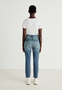 Bela majica s kratkimi rokavi, z gathered pasom, v kombinaciji z visokoračnimi modrimi kavbojkami, ki imajo dva zadnja žepa in podroženo denim zasnovo.