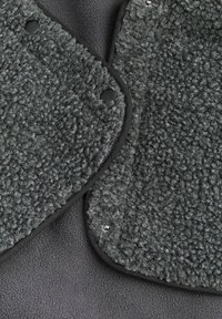 Šedá fleecová výplň má textúrovaný povrch s jemným, nadýchaným vzhľadom. Čierny lem obkolesuje okraje a uzatvára sa pomocou patentiek.