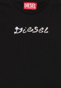 Juodas marškinėliai su sidabriniu metaliniu "Diesel" užrašu priekyje ir raudona etikete apykaklėje su prekės ženklu.