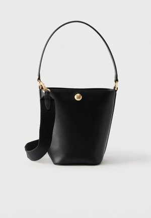 Čierna kožená bucket kabelka s krátkou rúčkou a širokým odnímateľným látkovým ramenným popruhom, na prednej strane s malým okrúhlym zlatým emblémom.