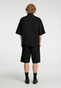 Camisa negra de manga corta con cuello, combinada con pantalones cortos negros. La tela parece suave con un ajuste relajado, sin patrones ni detalles visibles.