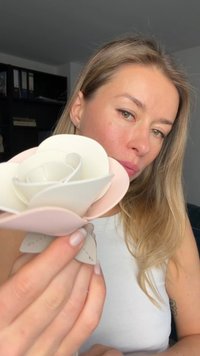 Une fleur en papier blanc et rose pâle, présentant des pétales superposés aux bords lisses, tenue contre un fond neutre.