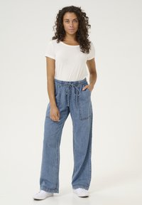 Gaišs, viegls T-krekls kombinēts ar ikdienišķām, brīvi pieguļošām, zilām džinsu biksēm ar aukliņu jostai un sānu kabatām.